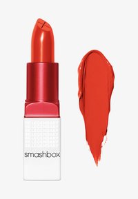 Lápiz labial rojo en un tubo plateado y blanco, con una punta en ángulo. Junto al producto hay una muestra de la misma tonalidad roja.