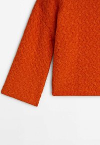 Gros plan de la manche orange en tricot d'un pull et du côté avec un motif texturé sur un tissu doux.