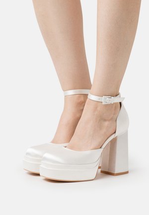 Hvide satin platform sko med en kraftig hæl, der har en ankelrem med spænde. Glat tekstur og afrundet frontdesign.