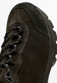 Dunkler Wildleder-Wanderschuh mit strukturierter Oberfläche, schwarzen Schnürsenkeln, Nahtdetails und einer robusten Gummisohle für Haltbarkeit.