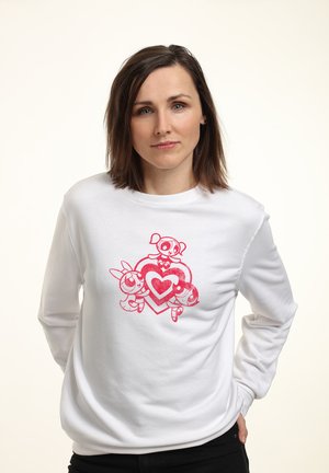 Biała bluza z dużym różowym grafiką przedstawiającą trzy postacie z kreskówek wokół wzoru serca. Długie rękawy z okrągłym dekoltem.