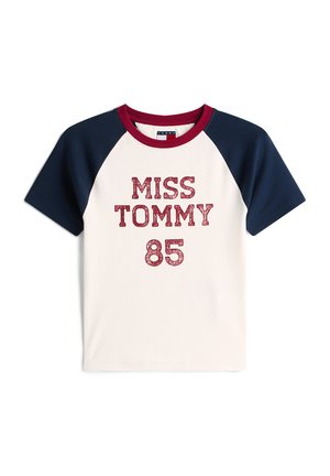 Medvilniniai marškinėliai su tamsiai mėlynomis raglano rankovėmis. Ant kreminio fono yra raudonas blizgantis užrašas „MISS TOMMY 85“. Apvalus kaklas.