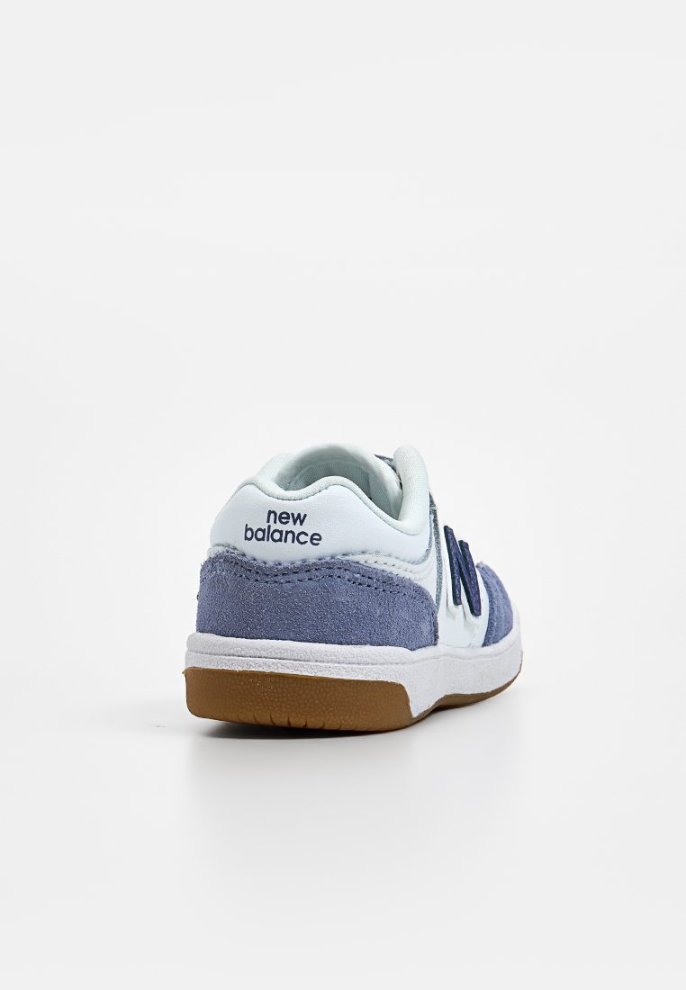 Sneaker con tomaia sintetica azzurro chiaro e accenti in suede grigio. Presenta una suola intermedia bianca e una suola esterna in gomma marrone. Logo "New Balance" sul tallone.