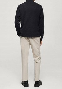 Pullover grigio scuro con colletto, abbinato a pantaloni beige su misura e scarpe nere. Il pullover ha una texture liscia e una vestibilità dritta.