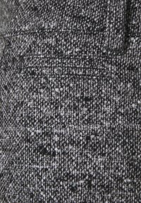 Zwart-wit gekleurd textiel met een gespikkeld patroon, voorzien van een subtiele zakdetail en een gladde afwerking.