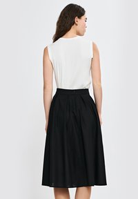 Biała bluzka bez rękawów połączona z czarną spódnicą do kolan, z plisami i widocznym zapięciem na suwak z tyłu.