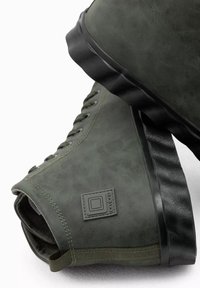 Baskets montantes synthétiques vertes avec une finition texturée, semelle en caoutchouc et coutures renforcées. Présente une patch de marque et un design à lacets.