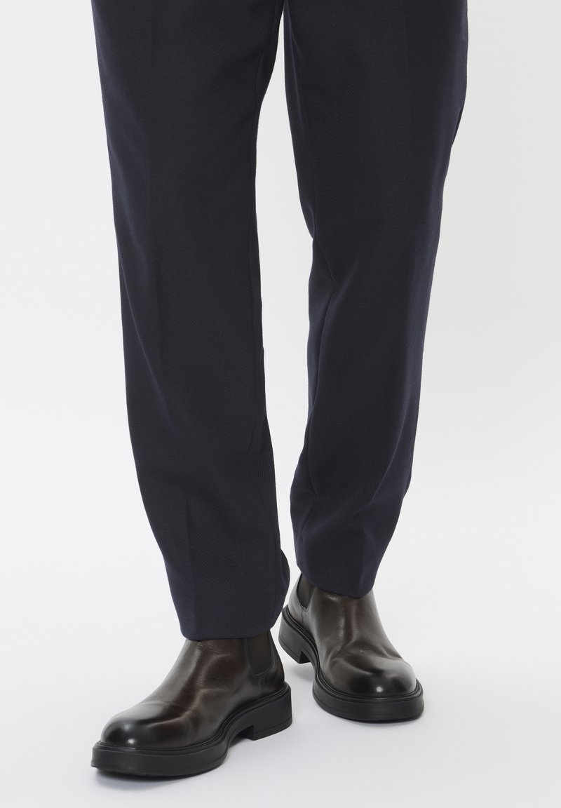 Pruunid nahast chelsea saapad läikiva viimistlusega, omavahel koos tumedad meresinised püksid, millel on täpselt sobiv lõige ja tekstuurne kangas.