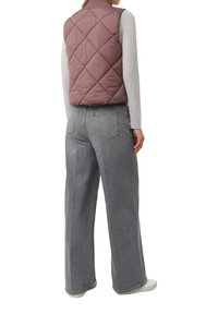 Gepolsterte, gestepptes Weste in staubigem Rosaton, kombiniert mit grauen weiten Jeans. Beide Kleidungsstücke zeichnen sich durch ein minimalistisches Design und weiche Texturen aus.