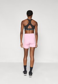 Μαύρο αθλητικό σουτιέν με σχεδιασμό κλειδαρότρυπας και σχέδιο στη ζώνη, σε συνδυασμό με ροζ εφαρμοστά σορτς, τονισμένα με πίσω τσέπες και λογότυπο.