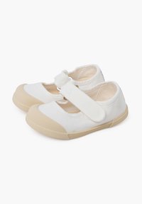Zapatos de lona blancos con punta redonda, suela de goma beige y una correa de velcro en el empeine. Presentan un diseño recortado.