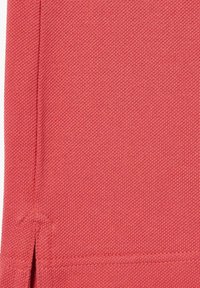 Tela de algodón coral con un tejido texturizado y aberturas laterales en el dobladillo; acabado limpio con detalles de costura reforzada.