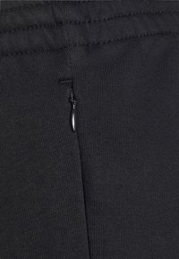 Čierna bavlnená tkanina s hladkou textúrou, so malým detailom zipsu na boku pre zvýšenú funkčnosť.