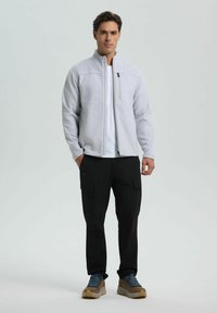 Světle šedá fleecová bunda na zip s vysokým límcem, doplněná černými cargo kalhotami a hnědými turistickými botami s modrými akcenty.