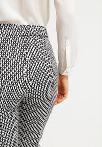 Zwart-witte, gemêleerde broek met een geometrisch patroon, met een aansluitende pasvorm en een soepele tailleband. Strak wit lange mouwen top.