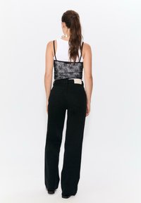 Svart vida jeans i kombination med en svart croptop med spetsdetaljer och en vit linne under, med justerbara band och en slät textur.