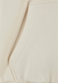Beige fabric close-up featuring a kangaroo pocket, with visible stitching and a soft texture. Simple design, no patterns or embellishments.
