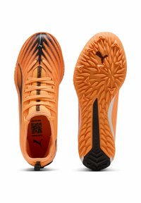 Scarpe da calcio arancione brillante con tomaia in rete intrecciata, accenti neri e suola in gomma testurizzata con tacchetti piramidali. Marchio ben visibile.