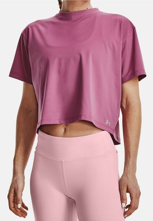 Frau trägt ein lockeres, kurzärmeliges Crop-Top in Mauve und hoch taillierte hellrosa Leggings, steht vor einem einfarbigen Hintergrund.