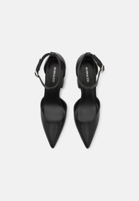 Black faux leather high-heeled shoes with a pointed toe and ankle strap, featuring a block heel and smooth texture. Logo visible inside.