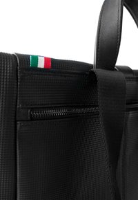 Schwarze, strukturierte Handtasche mit Reißverschluss, Lederakzenten und einem kleinen italienischen Flaggenmotiv oben. Robustes Design mit stabilen Griffen.