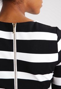 Détail d'une robe à rayures noires et blanches montrant un design ajusté, un tissu doux et une fermeture éclair métallique à l'arrière.