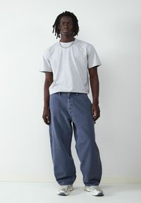 Szara bawełniana koszulka o luźnym kroju, zestawiona z luźnymi niebieskimi dżinsami. Warto zwrócić uwagę na srebrny łańcuszek i jasne trampki.