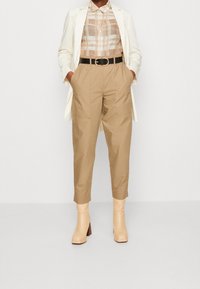 Pantalons beiges taille haute avec de grandes poches, associés à une chemise à carreaux beige et crème et un blazer blanc à rayures. Bottines beiges à talons.