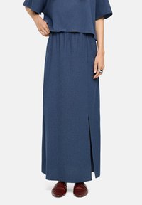 Niebieska maxi spódnica z teksturowanej tkaniny, z elastycznym paskiem w talii i bocznym rozcięciem, w połączeniu z czerwonymi butami wsuwanymi.
