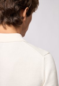 Maglione a maglia color beige chiaro con colletto a coste e design spalla senza cuciture, caratterizzato da una texture morbida e una finitura pulita all'orlo del collo.