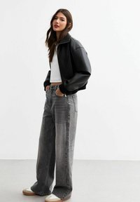 Chaqueta bomber de cuero sintético negra con puños acanalados, combinada con jeans de denim gris de corte holgado y zapatillas de color claro.