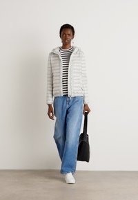 Lichtgrijze gewatteerde jas met horizontale naden, zwart-wit gestreept shirt, blauwe wijde jeans en witte sneakers. Zwarte schoudertas.