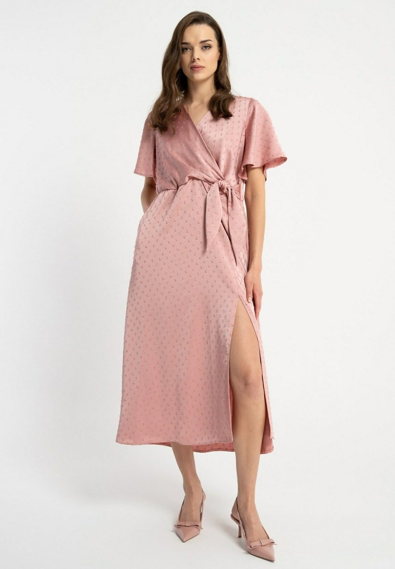 Różowa sukienka o fasonie kopertowym, wykonana z gładkiego materiału w delikatny wzór kropek, z krótkimi rękawami, wiązaniem w talii i rozcięciem z boku. W komplecie z pasującymi szpilkami.