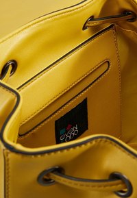 Intérieur d'un sac cabas en cuir jaune avec une texture lisse, comprenant une étiquette en tissu noire portant la mention "even & odd" et une poche fendue.