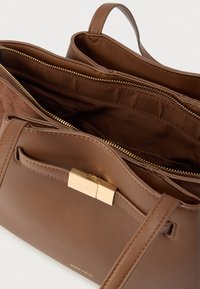 Barna bőr kézitáska sima textúrával, arany fém kiegészítőkkel és cipzáras belső zsebbel. Rövid felső fogantyúkkal.