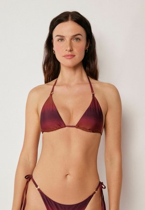 Frau mit langen dunklen Haaren, die ein burgunderfarbenes Ombre-Halfter-Bikinioberteil und passende Bikinihöschen mit seitlicher Krawatte vor einem einfarbigen Hintergrund trägt.