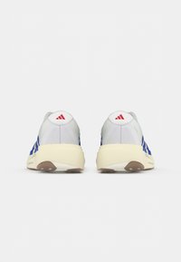 Baskets blanches avec des rayures bleues, dotées d'une semelle en caoutchouc blanc, d'un dessus en tissu texturé et d'un petit logo rouge sur le talon.