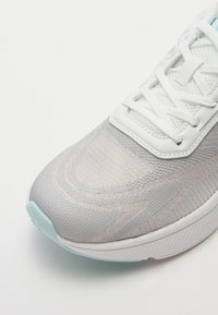 Chaussure de course légère avec une tige en maille dégradée grise et blanche, des lacets blancs et des accents bleu clair sur la semelle. Design à bout arrondi.