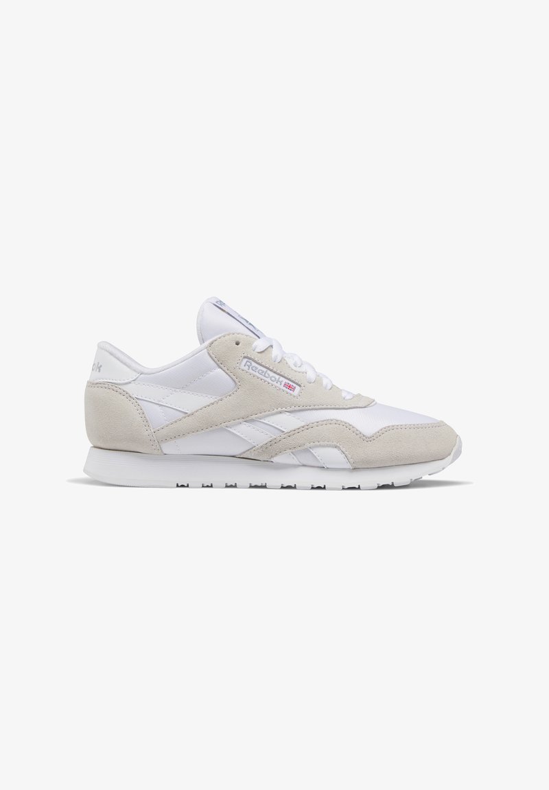Białe i beżowe sneakerzy Reebok z zamszowymi nakładkami, sznurowanym zapięciem i gumową podeszwą, przedstawione w profilu bocznym na białym tle.