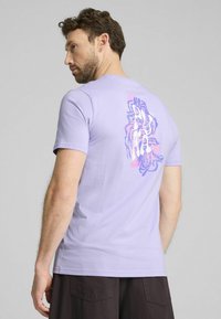 Lavendel bomulds t-shirt med et farverigt abstrakt design på ryggen, korte ærmer og rund halsudskæring.