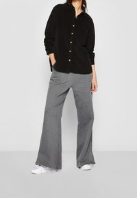 Schwarze Corduroy-Button-Up-Hemd mit einer Brusttasche, kombiniert mit weiten grauen Hosen und weißen Turnschuhen. Sanfte Textur, lockere Passform.