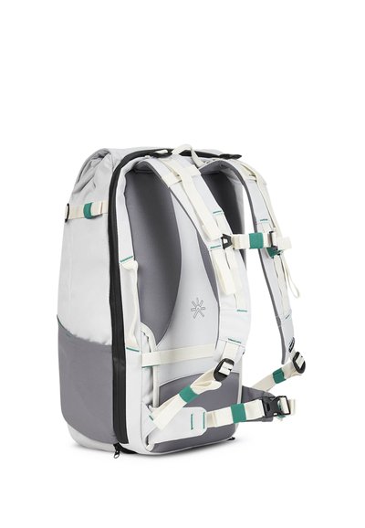 Mochila gris y blanca con correas acolchadas, múltiples ajustadores y una textura suave. Presenta un logo en el lado y un bolsillo con cremallera.