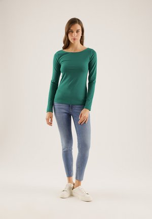 Langermet grønn topp med rund hals, parret med lyseblå smale jeans og hvite joggesko. Glatt tekstur, tettsittende design.