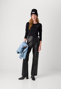 Svart langermet topp med logo, svarte skinnbukser med vide ben og svarte ankelstøvletter med hæl. Holder en lys blå denimjakke.
