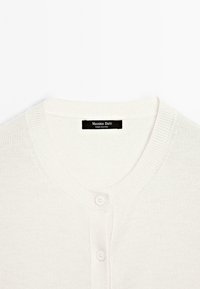 Maglione bianco con scollatura rotonda e due bottoni, con etichetta nera che riporta la scritta "Massimo Dutti" in un font semplice.