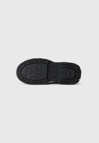 Suela de zapato de goma negra con surcos profundos que presenta la palabra "BUFFALO" repetida y un logo circular cerca del talón.