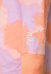 Långärmad skjorta i rosa och lavendeltoner med ett sprutmönster. Har en broderad "Nike"-logotyp på ärmslutet. Mjuk bomullsmaterial.