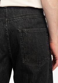 Černé džínové kalhoty s texturovaným povrchem, s kapsou na zadní straně a jemným šitím podél pasu a okrajů kapes.