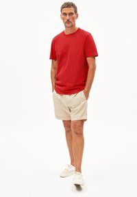 Rode katoenen t-shirt gecombineerd met beige shorts, voorzien van een elastische tailleband en zijzakken, aangevuld met witte sneakers.