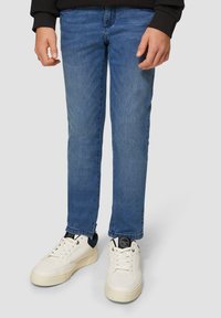 Niebieskie dżinsy o slim fit, zestawione z białymi trampkami z granatowymi akcentami. Trampki mają teksturowaną powierzchnię i sznurowadła.